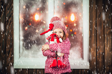 On Christmas night an adorable little girl near the window the snow falls.