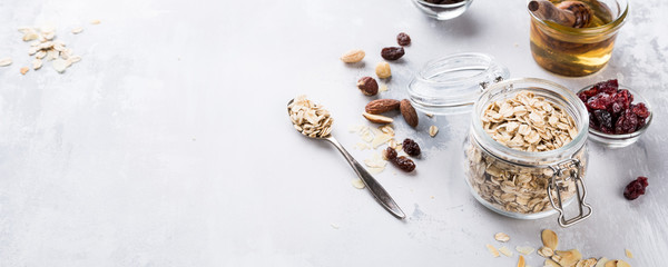 Ingredients for homemade oatmeal granola in glass jar. Oat flakes, honey, raisins and nuts. Healthy breakfast concept with copy space. Banner.