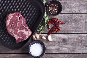 Ingredients for cooking healthy meat dinner. Raw uncooked beef steak on the iron grill pan with salt and pepper over wooden background. Top view. Copy space