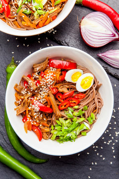 Noodles with chicken's meat, chili peppers and eggs in bowl on dark stone background. Asian Cuisine Pasta. Top view. 