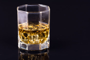 Octagon square glass with whiskey and ice cubes on the black background with reflections