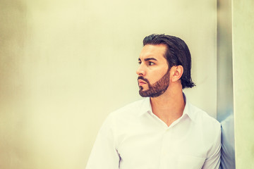 Portrait of Young Handsome American Man. Wearing white shirt, a guy with full beard standing against silver metal wall, looking away, waiting, expecting. Instagram filtered effect. Side View..