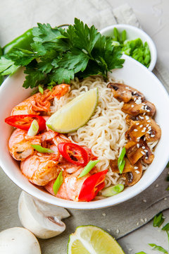 Noodles with shrimp, chili peppers and mushrooms in bowl on grey stone background. Asian Cuisine Pasta. Top view. 