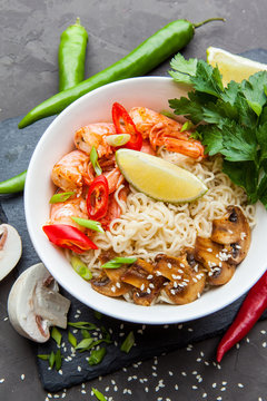 Noodles with shrimp, chili peppers and mushrooms in bowl on dark stone background. Asian Cuisine Pasta. Top view. 