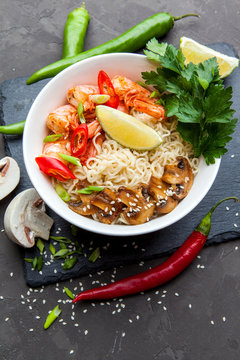 Noodles with shrimp, chili peppers and mushrooms in bowl on dark stone background. Asian Cuisine Pasta. Top view. 