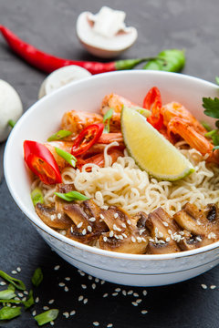 Noodles with shrimp, chili peppers and mushrooms in bowl on dark stone background. 