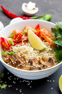 Noodles with shrimp, chili peppers and mushrooms in bowl on dark stone background. 