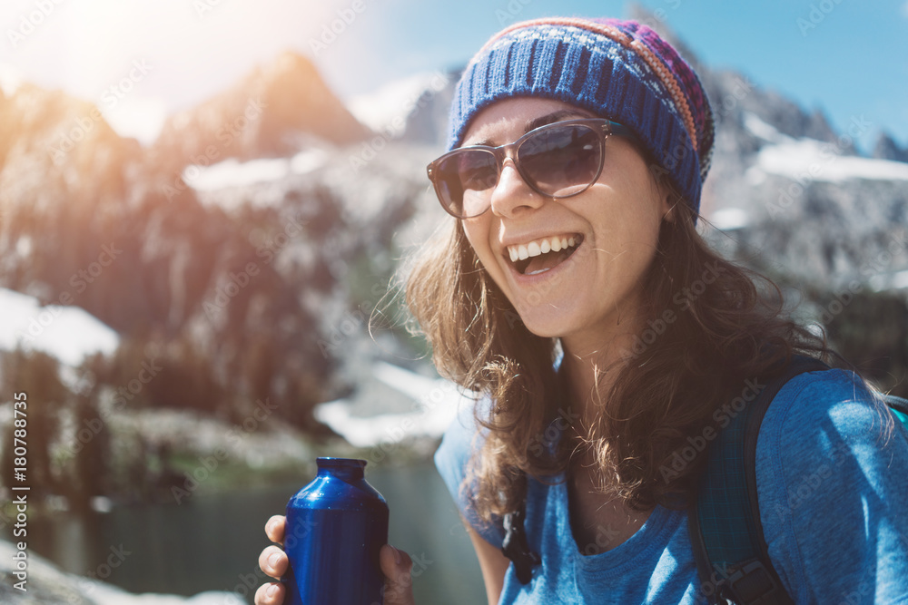 Wall mural portrait of handsome smiling hiking woman standing in stunning mountain wilderness with bottle near 