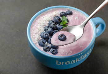 Blueberry yogurt with grated coconut on a dark stone table, close-up, selective focus