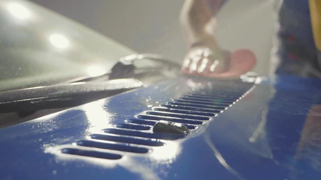 Close up of master polishing deep blue car in workshop, slow motion