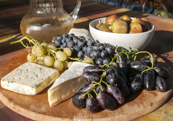 Wooden plateau with fresh grapes figs and types of cheese closeup as homefood background