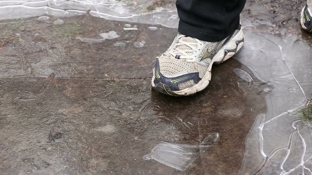 Man's foot crushing ice on puddle in winter