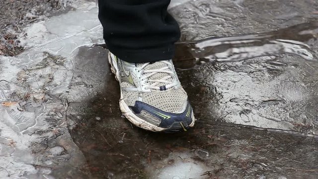 Man's foot crushing ice on puddle in winter