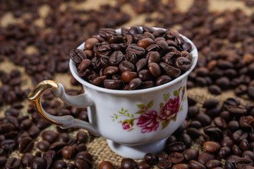 Coffee cup with purple flowers filled with beans surounded with beans on sackclothe