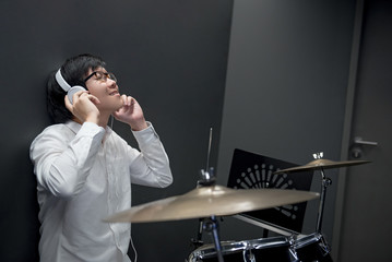 Young Asian man sitting with drum set annd enjoy listening to music in music practice room, musical therapy and musician lifestyle concepts