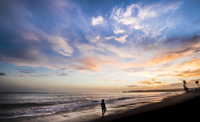 Woman walking along shoreline at sunset with beautiful sky above
