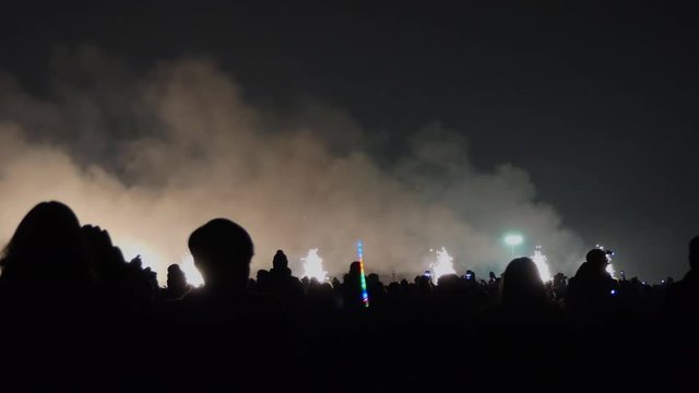 Many people watching and taking pictures of fireworks sparkling on the ground in cone shape before firework display in the sky