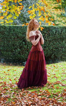 woman with long curly red hair wearing corset and tierd skirt with autumn leaves
