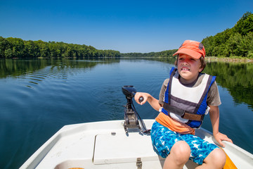 Lake, vacation, relaxation. Boy driving a boat with electric outboard motor on a lake in Poland....
