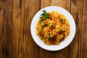 pilaf in a plate on wooden background, top view