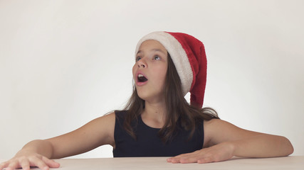 Beautiful happy girl teenager in a Santa Claus hat look and emotionally expresses a surprise on white background