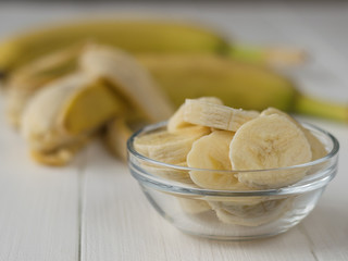 Pieces of ripe banana in the bowl on the background of the whole fruit.