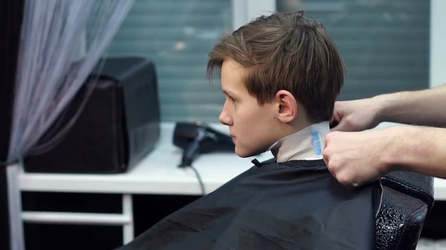 A male hairdresser puts on a young boy a protective cape before a haircut in the hairdresser. Close-up. Slow motion.