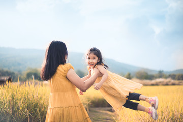 Cute asian child girl smile and fun while mother holding her kid and spinning around in the cornfield in vintage color tone