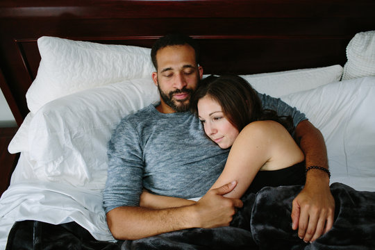 Black and white couple cuddling in bed