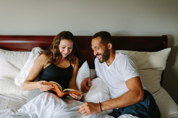 Happy mixed race couple in bed talking and reading a book