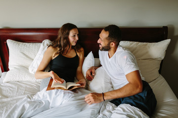 Happy mixed race couple in bed talking and reading a book