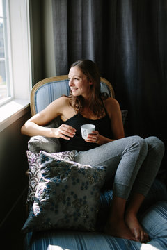 Happy woman sitting in a chair and looking out the window with her coffee