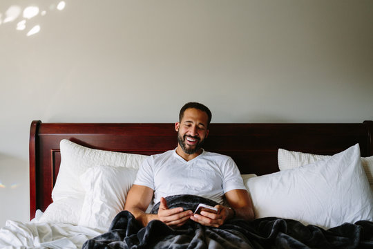 Black Man Working From Bed On His Phone