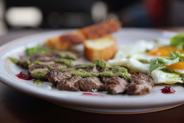 Grilled beef steak with toast , fried egg and vegetables on top with pesto sauce
