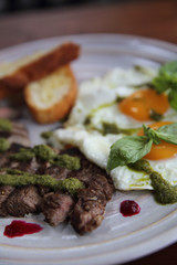 Grilled beef steak with toast , fried egg and vegetables on top with pesto sauce