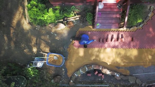 Aerial camera looking straight down showing a hardscape worker putting brick pavers into a herringbone pattern on a backyard patio project.