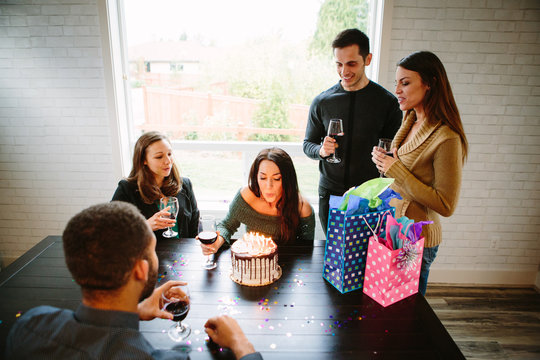 Woman Blowing Out Candles On Birthday Cake With Friends