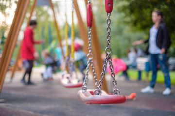 Modern equipped kids playground in sunny day. Kids and parents on chain swings