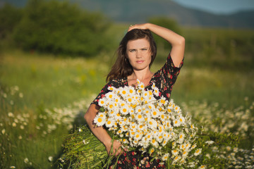 Naklejka na ściany i meble Charming adorable young lady woman dark brunette hairs and green eyes tender sexy posing with flowers wreath on head top and huge bouquet of wild daisy chamomile wearing stylish dress.