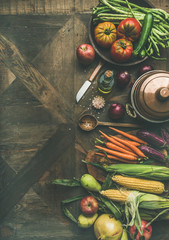 Fall cooking background. Autumn ingredients for Thanksgiving day dinner preparation. Flat-lay of green beans, corn cobs, carrot, tomatoes, eggplant, fruits over wooden table, top view, copy space