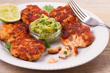 Salmon patties or cakes, lime and avocado on white plate. Fritters of fish. Salmon burgers. Healthy snack or take-away lunch bites