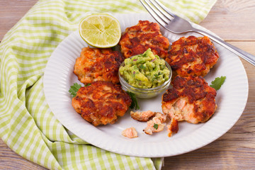 Salmon patties or cakes, lime and avocado on white plate. Fritters of fish. Salmon burgers. Healthy snack or take-away lunch bites