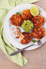 Salmon patties or cakes, lime and avocado on white plate. Fritters of fish. Salmon burgers. Healthy snack or take-away lunch bites, overhead