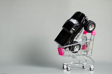 Miniature car pickup truck with stacks of coins on shopping cart or supermarket trolley on grey background with copy space, banking savings money and business finance concept. © pookpiik