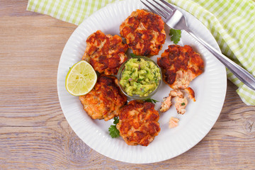 Salmon patties or cakes, lime and avocado on white plate. Fritters of fish. Salmon burgers. Healthy snack or take-away lunch bites, overhead