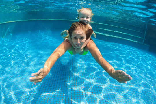 Funny portrait of child learn swimming, diving in blue pool on mother back - jumping deep down underwater. Healthy family lifestyle, kids water sports activity, swimming lesson with parents.