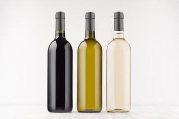 Three wine bottles  different colors - transparent, green, black- on white wooden board, mock up. Template for advertising, design, branding identity.