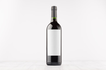 Dark wine bottle with blank white label on white wooden board, mock up. Template for advertising, design, branding identity.