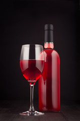 Bottle of rose wine and wine glass mock up on elegant dark black wooden background, vertical.