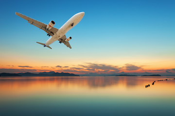 Airplane flying over tropical sea at beautiful sunset or sunrise scenery background.